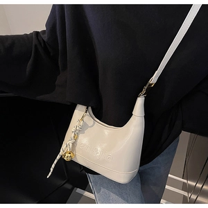 Detail of white half-moon bag featuring embossed logo and golden bell charm ornament