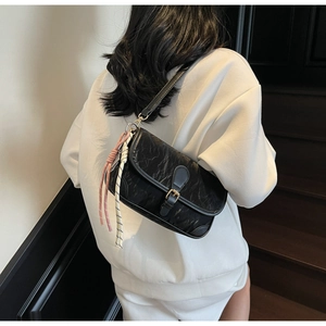 Detail of black pleated shoulder bag featuring metal buckle and decorative cords