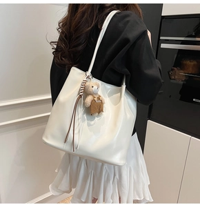 Detailed view of white glossy leather tote bag with cute bear charm and woven tassel detail