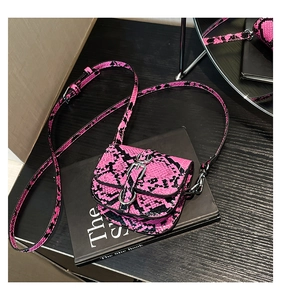 Close-up of pink and black snakeskin mini saddle bag with silver buckle on a book