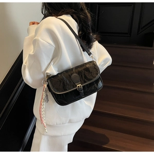 Detail of black pleated shoulder bag featuring a gold buckle and woven side ornament