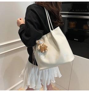 Close-up of white leather tote bag with a cute bear charm on model in a home setting