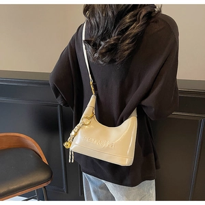 Detail of cream hobo bag with gold metal rings and embossed logo on model's shoulder