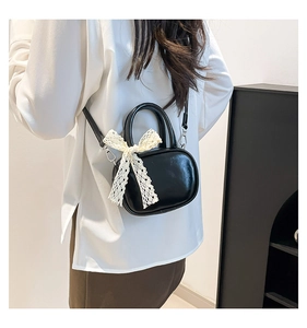 Detail of black glossy mini bag with white lace bow accent and detachable shoulder strap