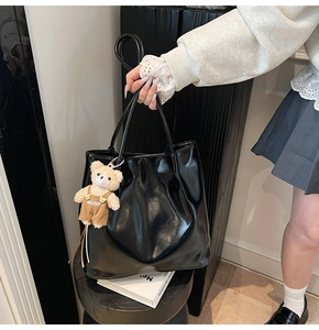Detailed view of large black glossy leather tote bag with a cute teddy bear charm