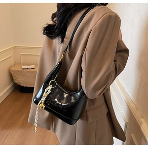 Detail of black glossy hobo bag with gold hardware and woven charm accessory
