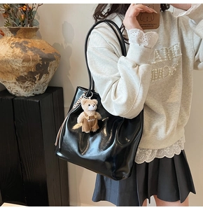 Detail of black glossy leather tote bag with a cute bear plush and tassel charm