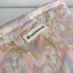 Detalle de la textura jacquard floral y la etiqueta de la marca en la bolsa de cosméticos