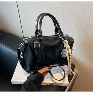 Detail of black glossy Boston bag with tennis racket charm and soft leather texture