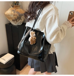 Detail of a large black glossy leather tote bag with a cute plush bear charm and woven rope