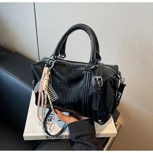 Detalle de bolso Boston negro brillante con colgante de ábaco plateado y cuerda trenzada