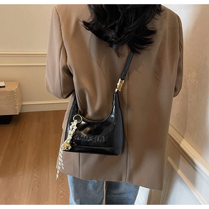 Detailed view of black leather hobo bag with embossed logo and woven charm accessory