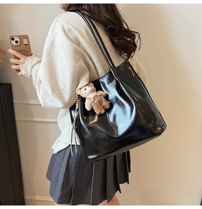 Detail of black patent leather tote bag with a cute plush bear pendant and shoulder strap