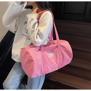 Dettaglio borsa da viaggio in nylon rosa con ricamo WE su una scala in legno scuro