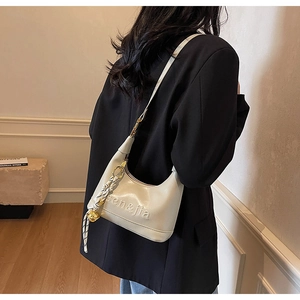 Detail of a creamy beige crescent underarm bag with a gold bell charm and embossed logo