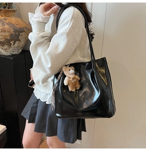 Detail of a large black glossy leather tote bag with a cute bear charm pendant