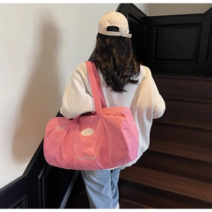 Dettaglio della borsa da viaggio in tela rosa con ricamo WE indossata sulle scale