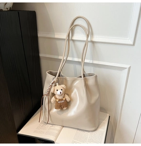 Detail of a beige leather tote bag with a cute bear charm on an open book