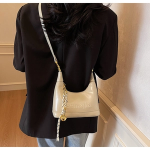 Detail of cream crossbody dumpling bag with letter embossing and decorative charm