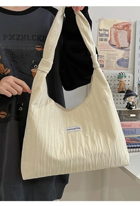 Close-up of beige tote bag with vertical pleats and brand label on a model's shoulder