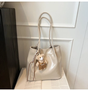 Detail of off-white faux leather tote bag with cute plush bear charm on a magazine