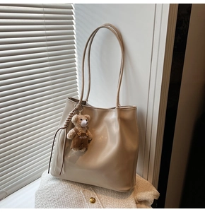 Detail of a large cream tote bag with a cute bear pendant on a white tweed garment