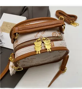 Close-up of golden bear-shaped dual zippers on a cream retro boston bag with brown trim