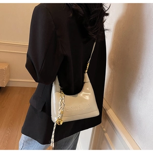 Detail of glossy beige shoulder bag featuring embossed logo and unique rope charm decoration