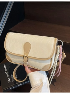 Chic beige textured crossbody bag with brown trim and woven charm on a wooden background
