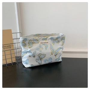 Detailed view of butterfly print makeup bag with gold outlines and zipper on wooden desk
