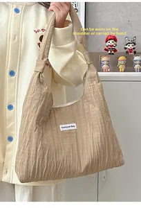 Detail showing beige pleated fabric texture and white brand label on hobo tote bag