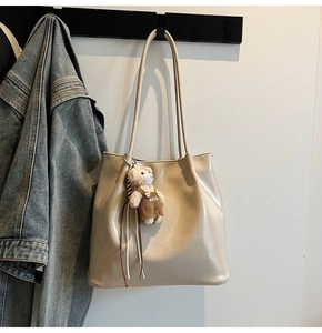 Close-up of beige glossy tote bag with dual straps and cute bear doll charm detail