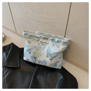 Close-up of butterfly embroidery and metal zipper on woven fabric makeup bag