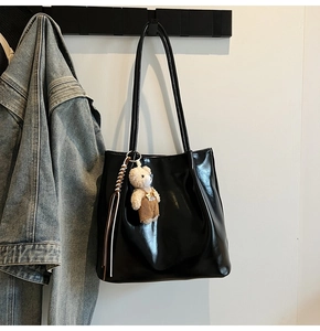 Detail of a black shiny leather tote bag featuring a cute plush bear charm with BUMP text