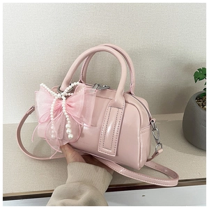 Gros plan du sac Boston en cuir verni rose avec nœud en organza et perles blanches
