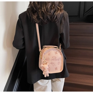 Detail of a pink textured leather backpack featuring cartoon bear prints and a plush charm