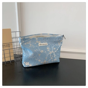 Detail of light blue floral jacquard makeup bag with zipper and woven brand label