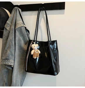 Detail of glossy black tote bag with long straps and a cute brown bear charm hanger