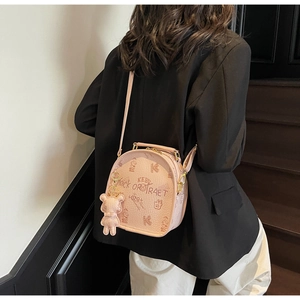 Rear view of a stylish pink round crossbody bag with bear pendant worn with black blazer