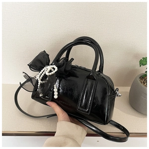 Détails du sac à main en cuir verni noir avec nœud en résille et breloques perles