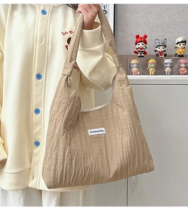 Detail of khaki pleated tote bag with white branded label shown in a cozy indoor setting