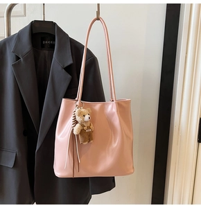Detail of pink faux leather tote bag featuring a cute plush bear charm on a grey blazer