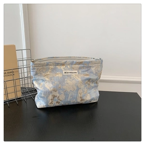 Close-up of blue and gold woven makeup bag with metal zipper on a dark wood desk