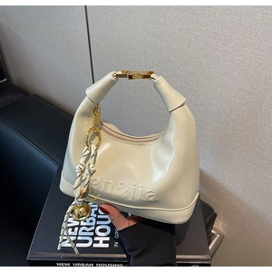 Detail of cream leather hobo bag with embossed logo and gold sphere woven pendant