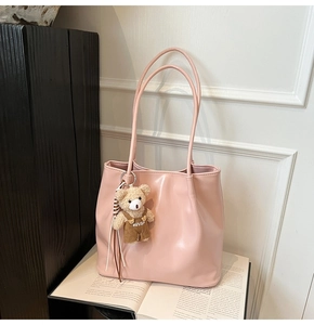 Detailed view of pink glossy leather tote bag featuring a cute plush bear charm with embroidery