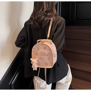 Close-up of pink textured faux leather backpack with bear charm on a female model