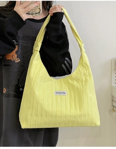 Detailed view of bright yellow pleated tote bag featuring a knotted handle and fabric label