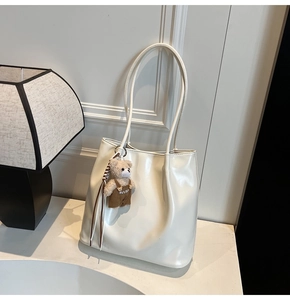 Close-up of white glossy tote bag featuring a cute brown plush bear charm and long straps