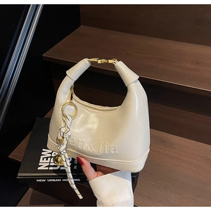 Detail of white glossy leather handbag with letter embossing and striped tassel charm
