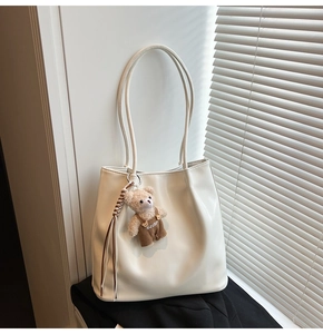 Detail of off-white PU leather tote bag with a cute bear charm and woven tassel accent